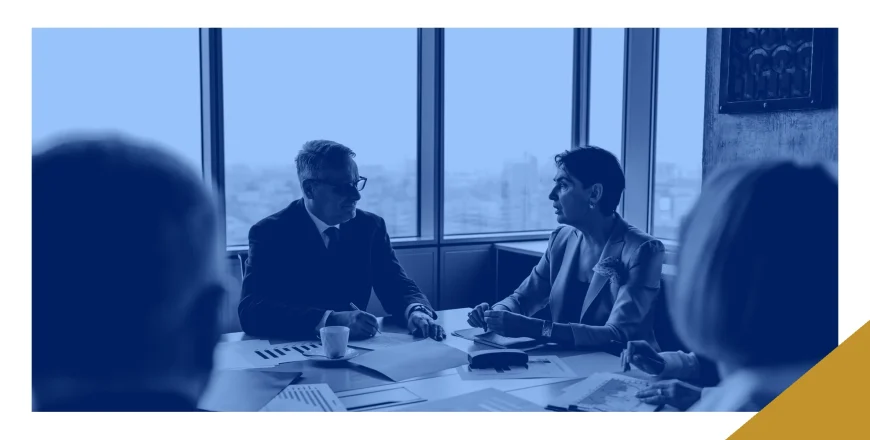 Two executives reviewing printed financial documents across a boardroom table while colleagues sit in on the discussion